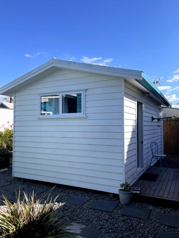a small white house with a wooden deck at Papamoa Beach Sleepout in Papamoa