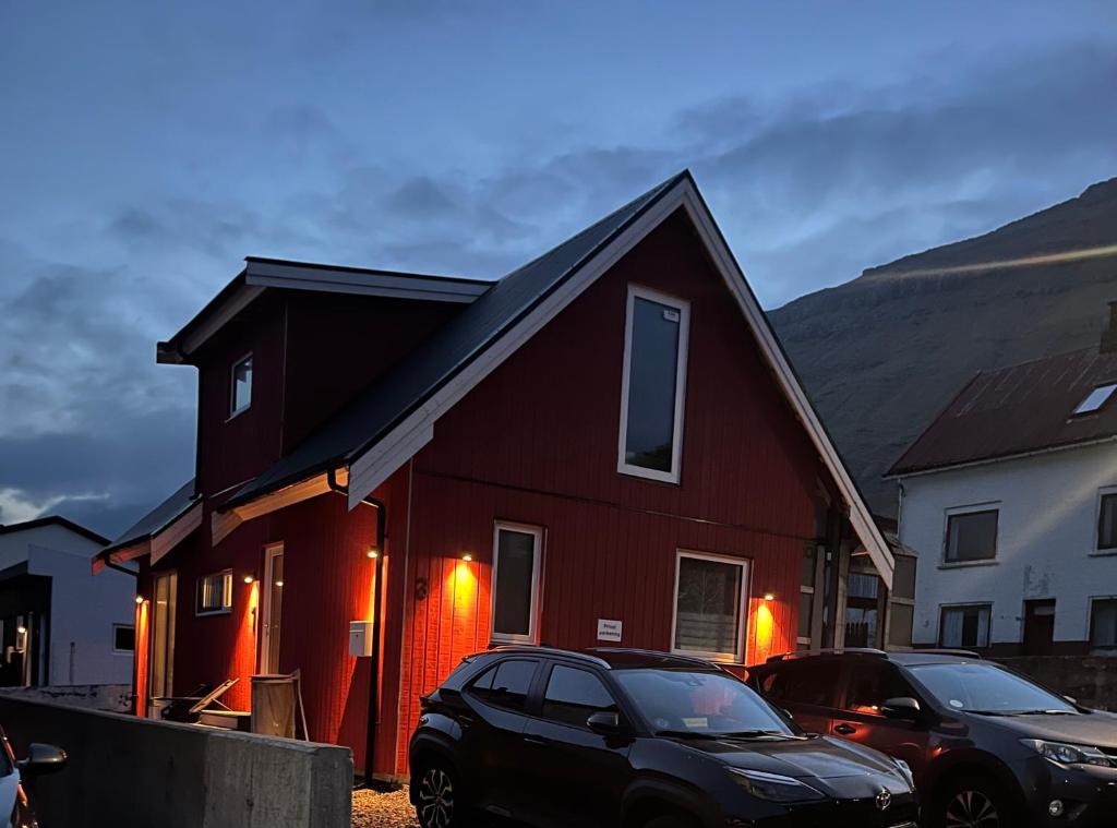 a red house with two cars parked in front of it at Vacationhouse in Klakvik in Klaksvík