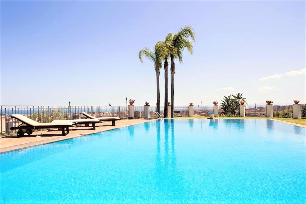 a large blue swimming pool with palm trees and the ocean at Casa Dimora Vittoria in Catania