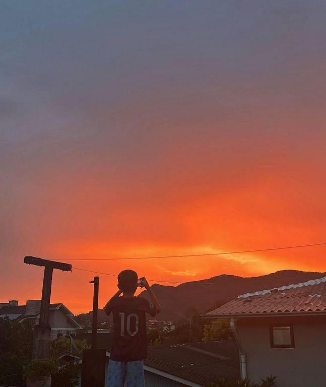 a boy standing on a balcony looking at the sunset at Hostel e Pousada das Rosas Nova Hartz RS in Nova Hartz