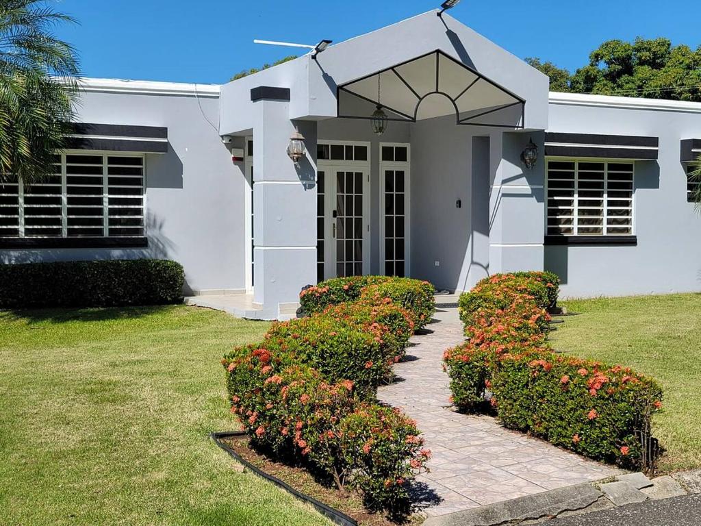 a white house with bushes and flowers in front of it at Villa in Miradero in Mayaguez