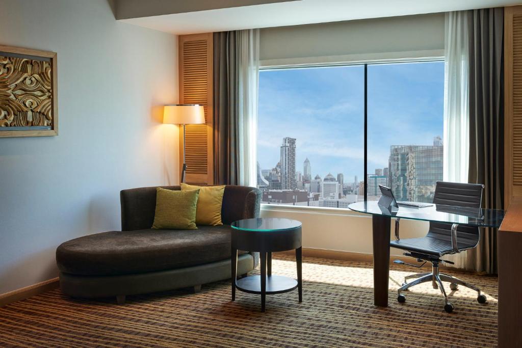 A suite sitting area with a chaise sofa, work desk, and broad city view.