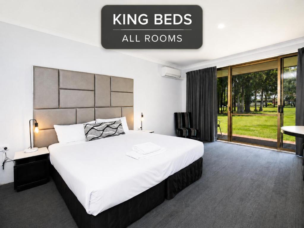 a bedroom with a king bed with a sign that reads king beds all rooms at Island Palms Motor Inn in Forster