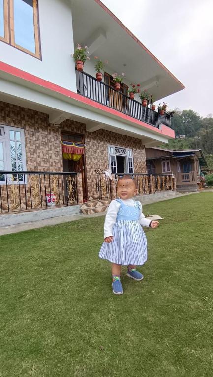 a small child standing in the grass in front of a house at Dhim in Mangpu