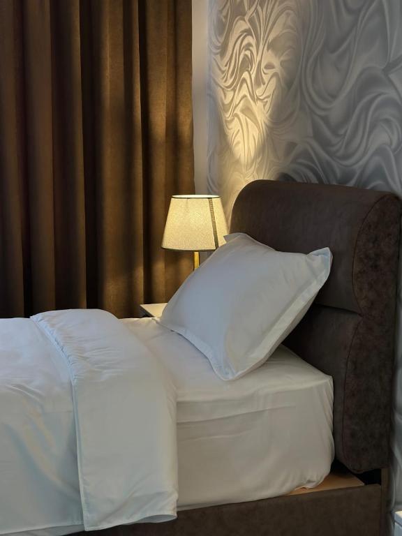 a bed with white sheets and pillows next to a lamp at Karibi in Kyzylorda