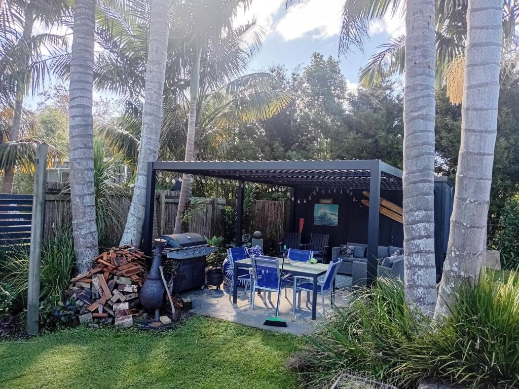 a patio with a grill and chairs and palm trees at Mangawhai Palms in Mangawhai