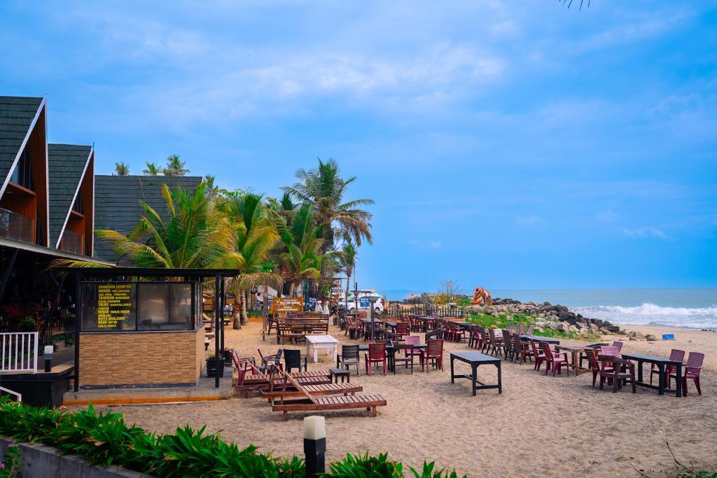 a sandy beach with tables and chairs and a restaurant at West Bay Palm Tree Beach Resort in Varkala