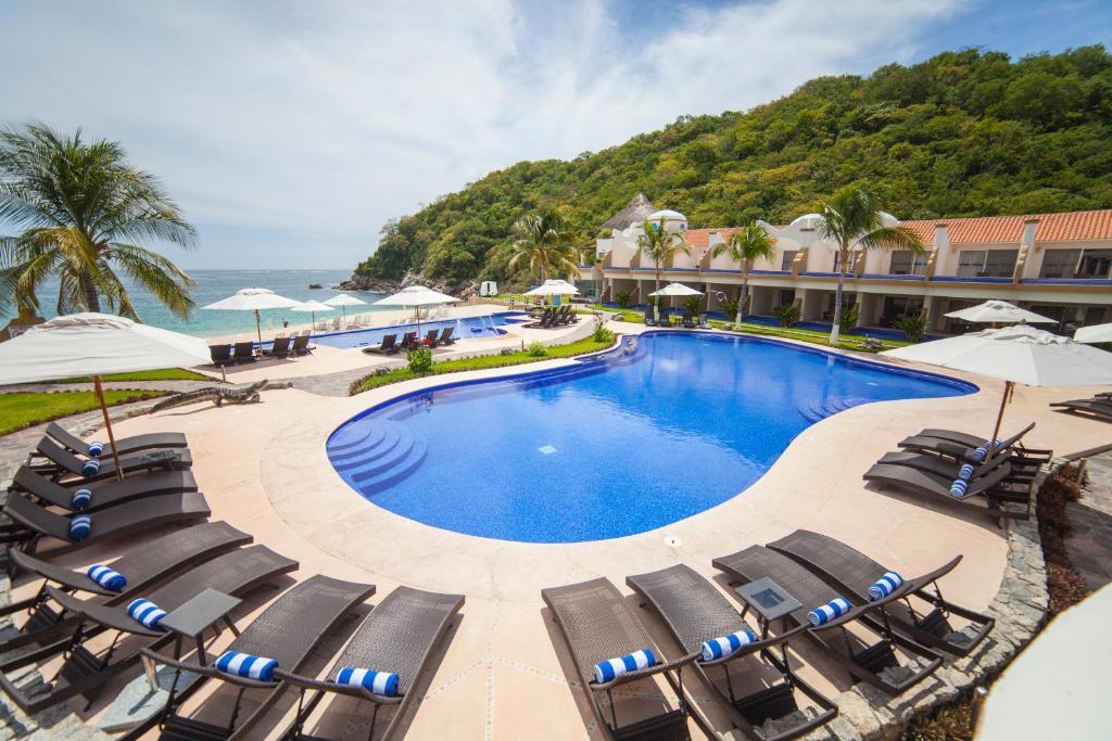 una piscina con sedie e ombrelloni accanto all'oceano di Quinta Bella Huatulco a Santa Cruz Huatulco