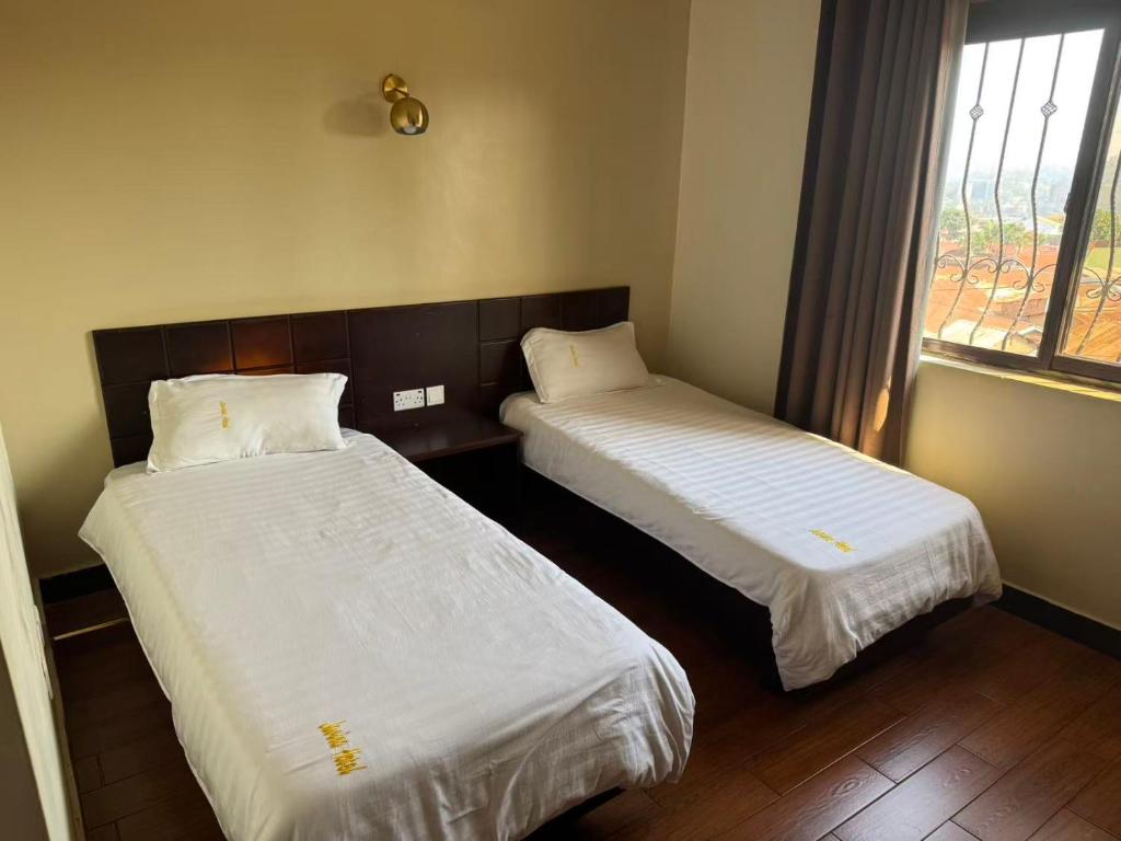 two beds in a room with a window at Kibuli beijing hotel in Kampala