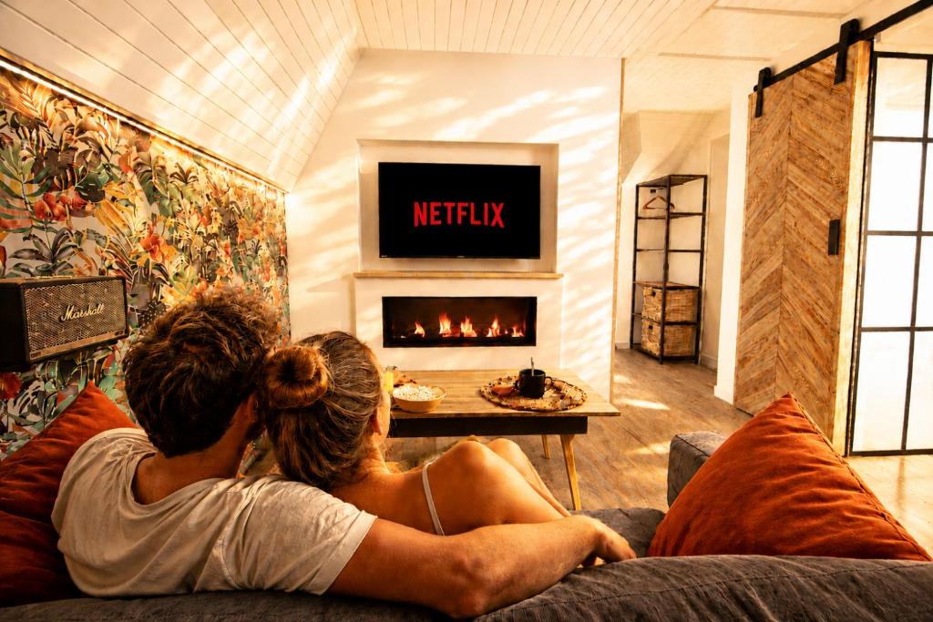 a couple sitting on a couch in front of a fireplace at MRODBNB - Appart Neuf - Vue Mer - 25m Plage & Resto - Ciné - cheminée - Popcorn in Cancale