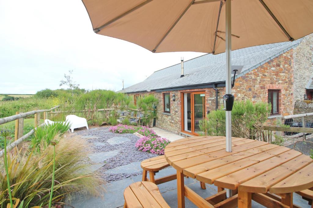 a wooden table with an umbrella in front of a house at Attractive barn conversion near Padstow in Saint Merryn