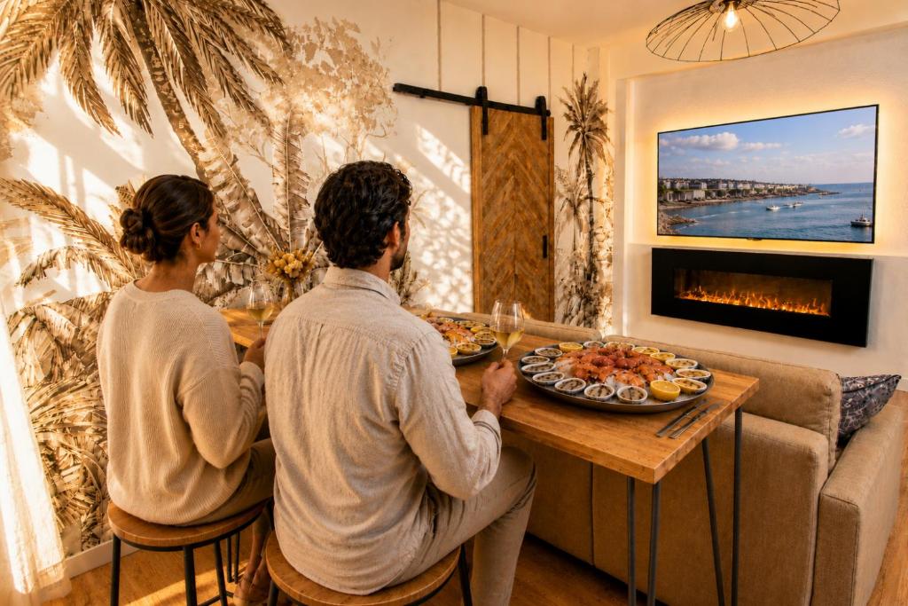 a man and woman sitting at a table in a living room at MRODBNB - Appart Neuf - Aperçu Mer - 25m Plage & Resto - Ciné - Cheminée - Popcorn in Cancale
