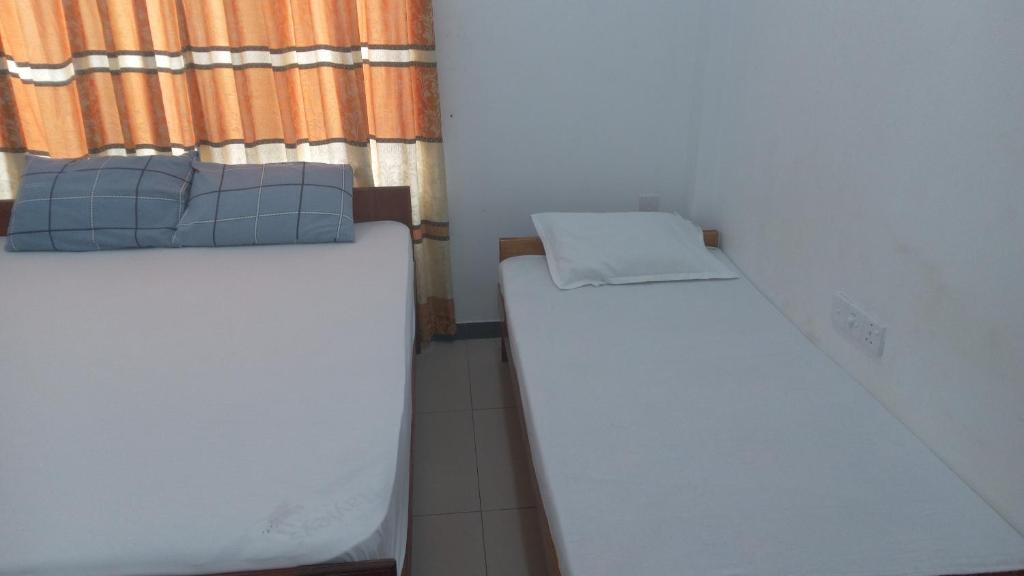 two beds in a small room with a window at Bhaavi Guest Inn in Jaffna