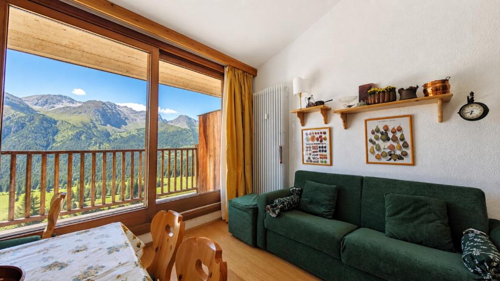a living room with a green couch and a large window at Hostdomus - Sansicario R20 in San Sicario