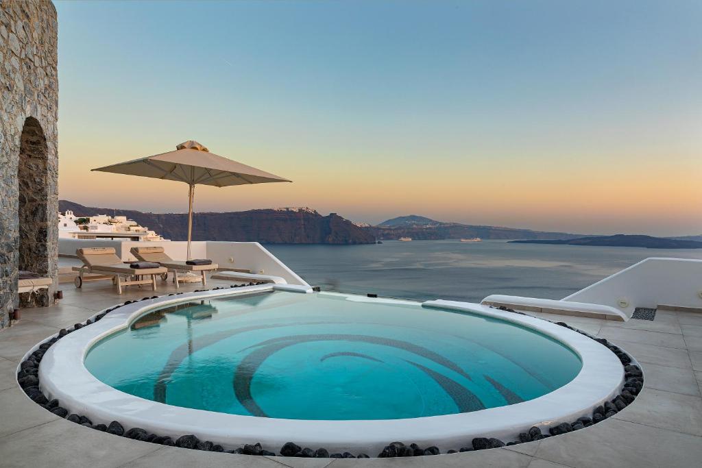 a swimming pool with an umbrella and a view of the ocean at Santorini Secret Premium in Oia