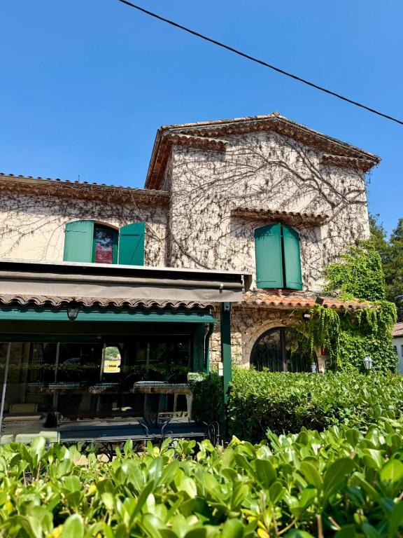 a stone building with green shuttered windows and bushes at L'Imprevisto in Grasse
