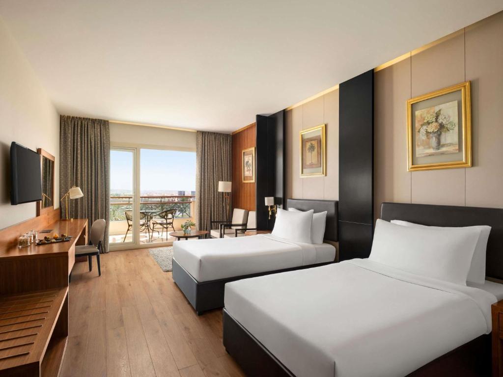 a hotel room with two beds and a desk at Mövenpick Hotel Cairo - Media City in 6th Of October