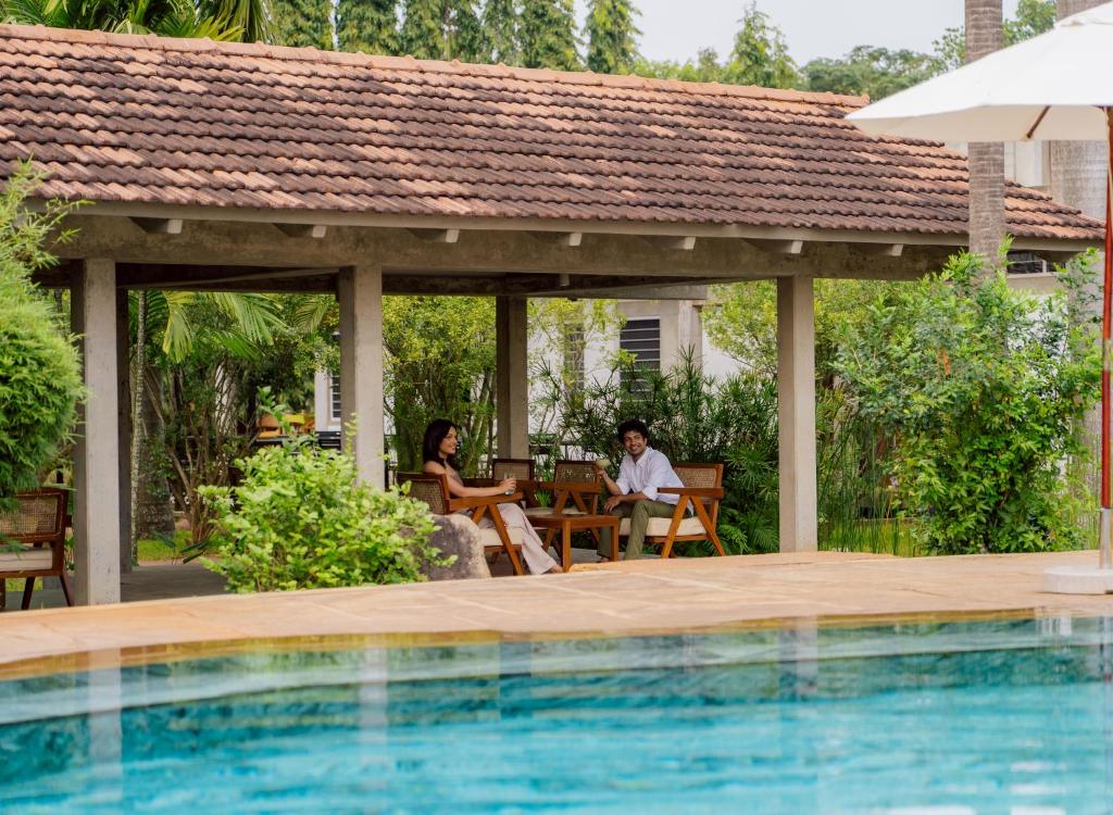 two people sitting at a table next to a swimming pool at Sanctuary Amaidiyana - A CGH Earth Experience in Pondicherry