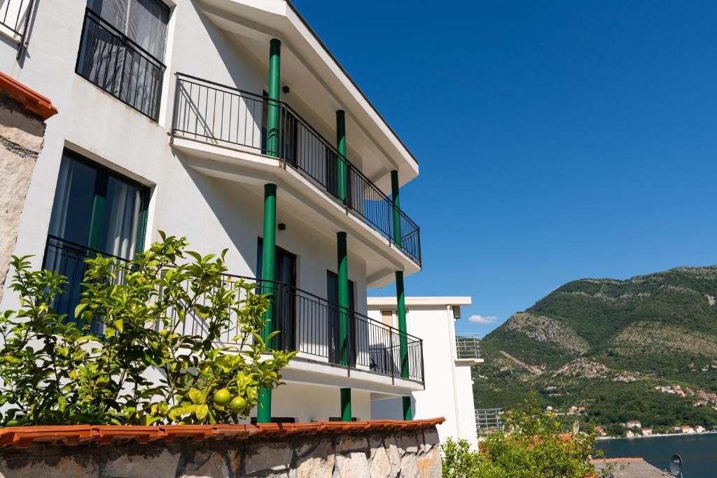 a white building with green windows and a tree at Apartmani Natal in Donja Lastva