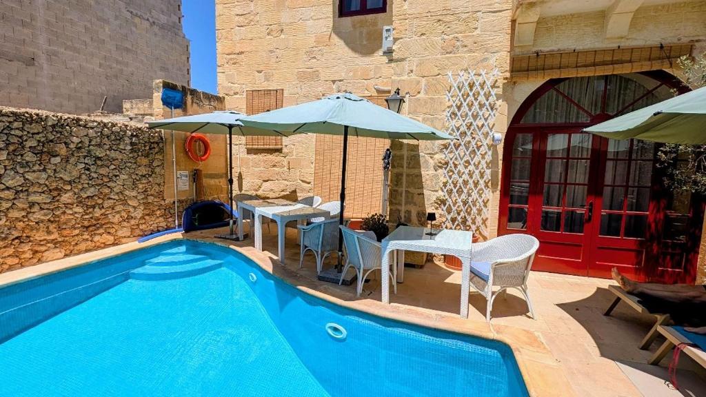 a swimming pool with tables and chairs and umbrellas at Razzett Pepprina Poppy Farm in Xagħra