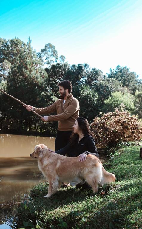 a man and a woman and a dog by a river at Hotel Cabanas Glamour in Gramado