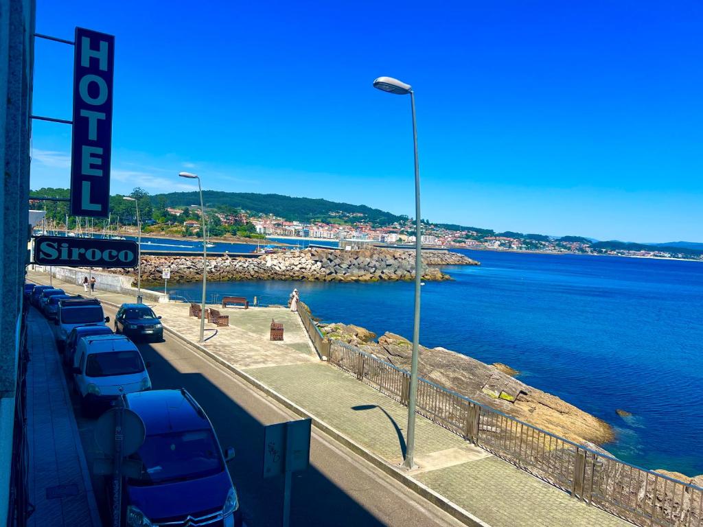 a row of cars parked on a road next to the water at Hotel Siroco Portonovo in Sanxenxo