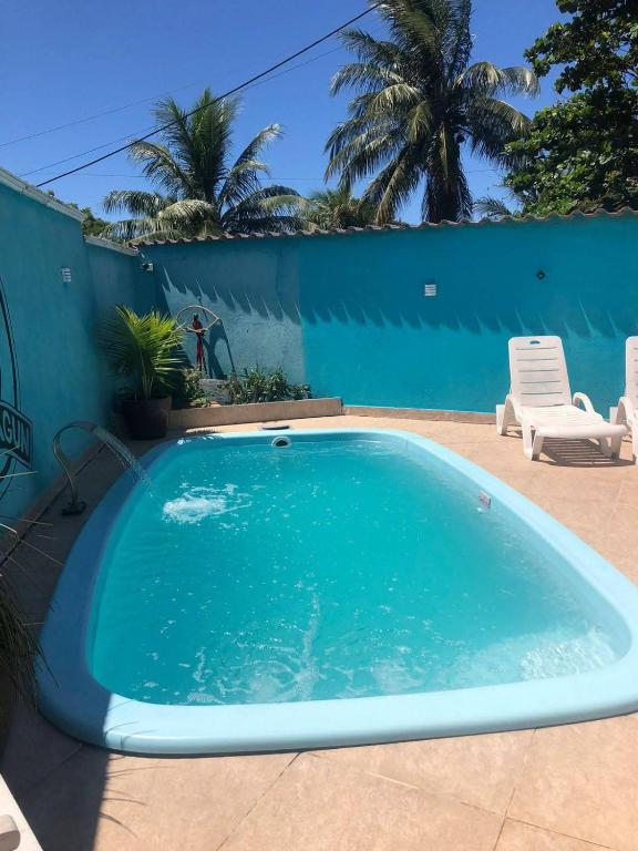 a swimming pool in a yard with a blue wall and palm trees at Quarto,cozinha,banheiro e área externa compartilhada in Araruama