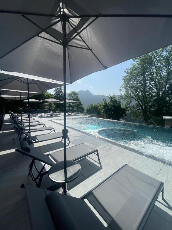 Eine Gruppe von Stühlen und Sonnenschirmen neben einem Schwimmbecken in der Unterkunft Hotel Central Résidence & spa in Leysin