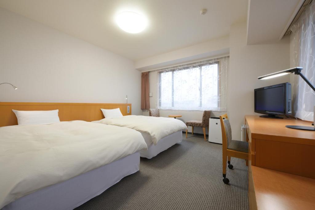 a hotel room with two beds and a desk and a television at Grand Park Hotel Odate in Odate
