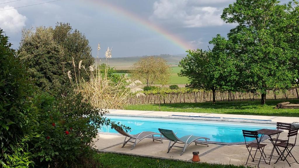 a pool with chairs and a rainbow in the background at La Belle Echappée in Champagnac