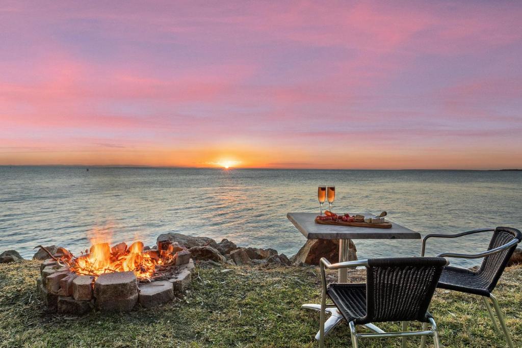 a fire pit next to the water with a table and chairs at Allies Place in Amity Point