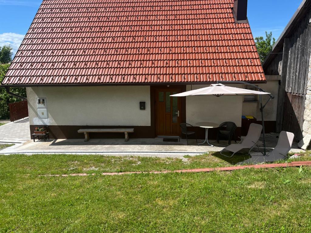 a house with an umbrella and a table and a bench at Apartma Hiška Vrh in Stari Trg pri Ložu