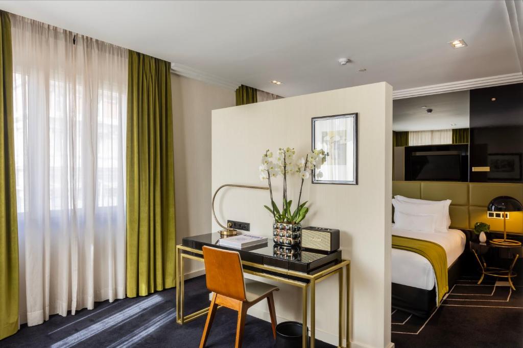 A compact writing desk with an orange chair, orchid arrangement and a bedroom visible behind it.
