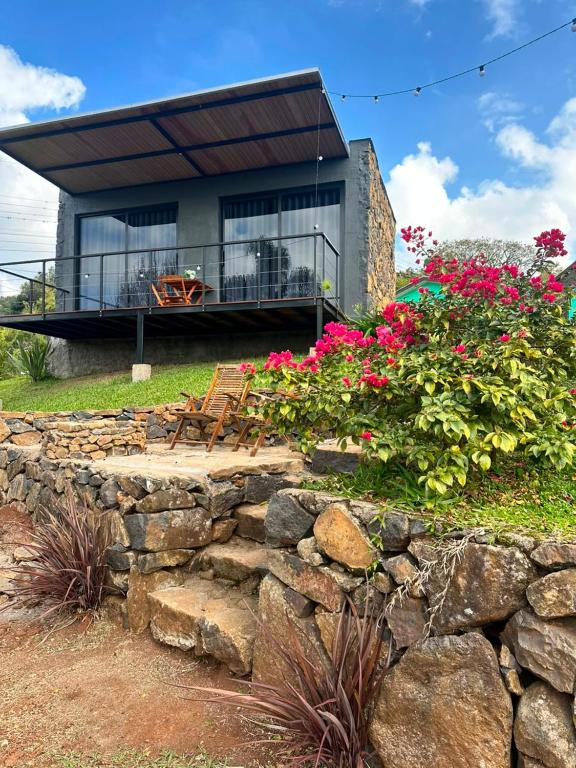a house with a stone wall and some flowers at Cabana Chácara Vilagio daspedras in Nova Petrópolis
