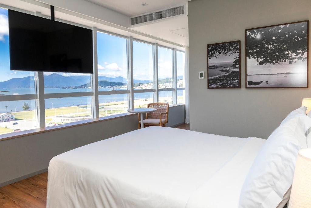 ein Schlafzimmer mit einem großen weißen Bett und einem großen Fenster in der Unterkunft K-Platz Florianópolis São José in São José