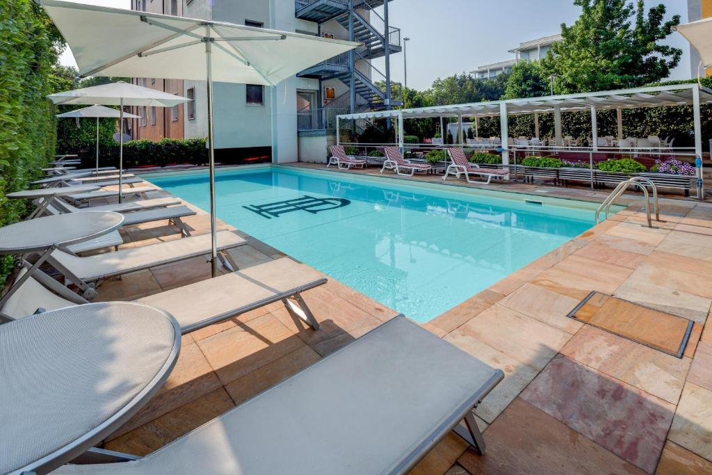 ein Schwimmbad mit Liegestühlen und Sonnenschirmen neben einem Gebäude in der Unterkunft Jet Hotel, Sure Hotel Collection by Best Western in Gallarate