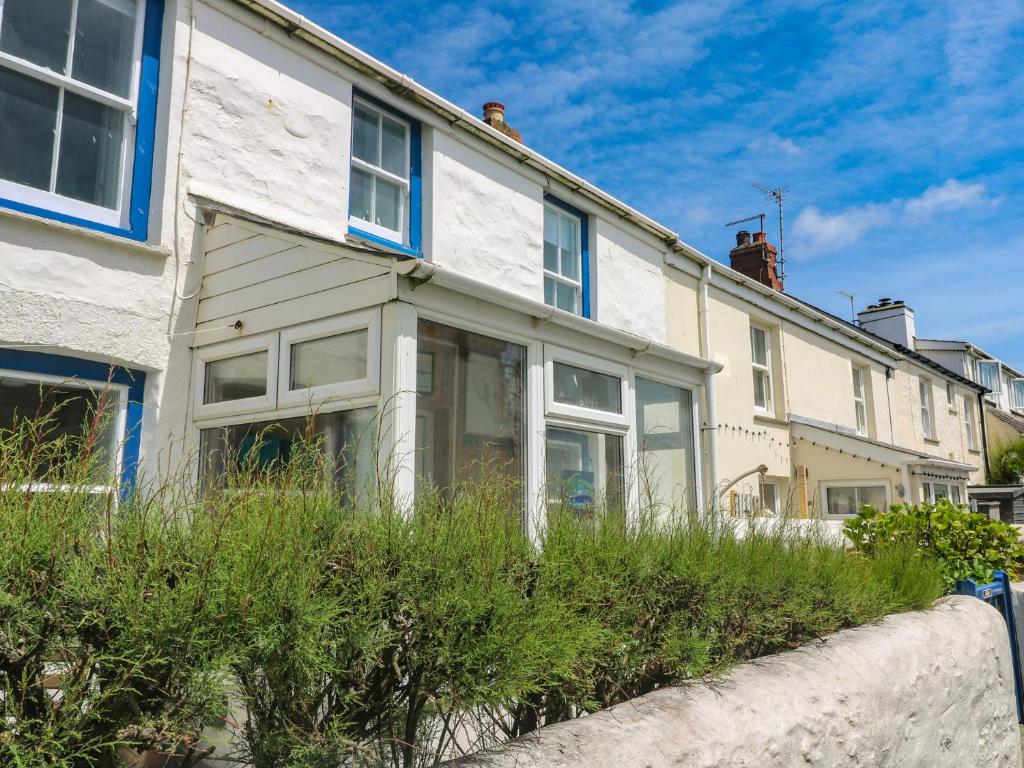 a white house with blue windows and bushes at Pegs in Porthleven