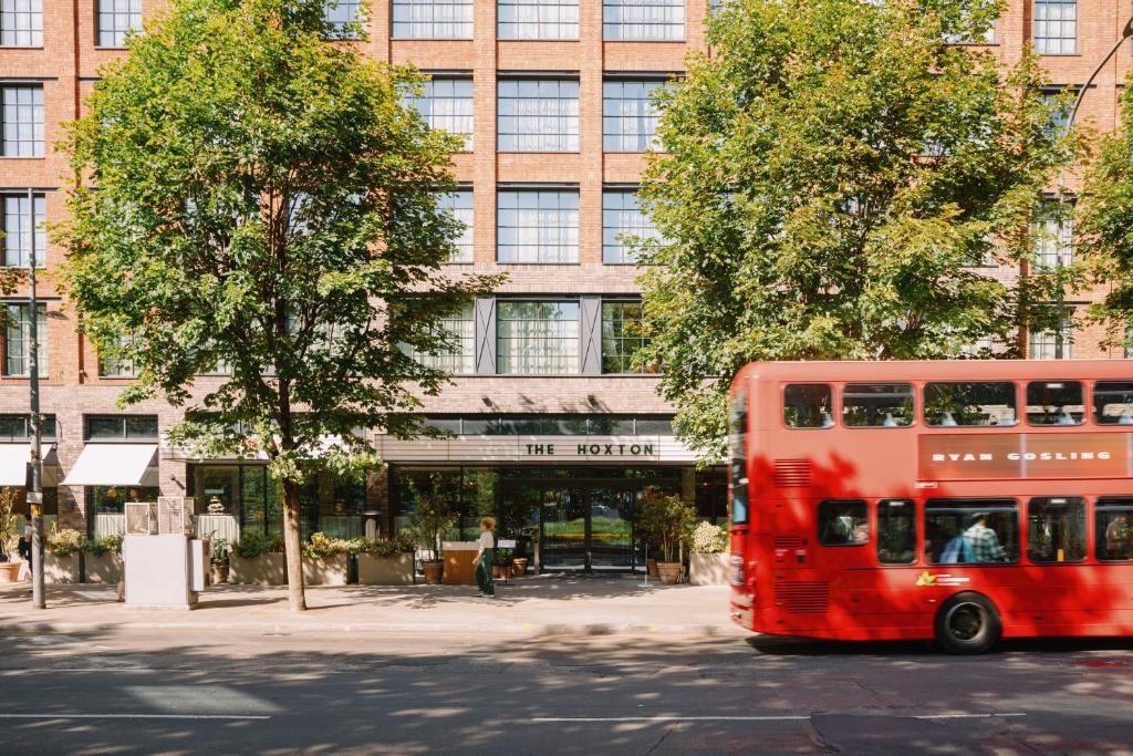 a red double decker bus driving past a building at The Hoxton, Shepherds Bush in London