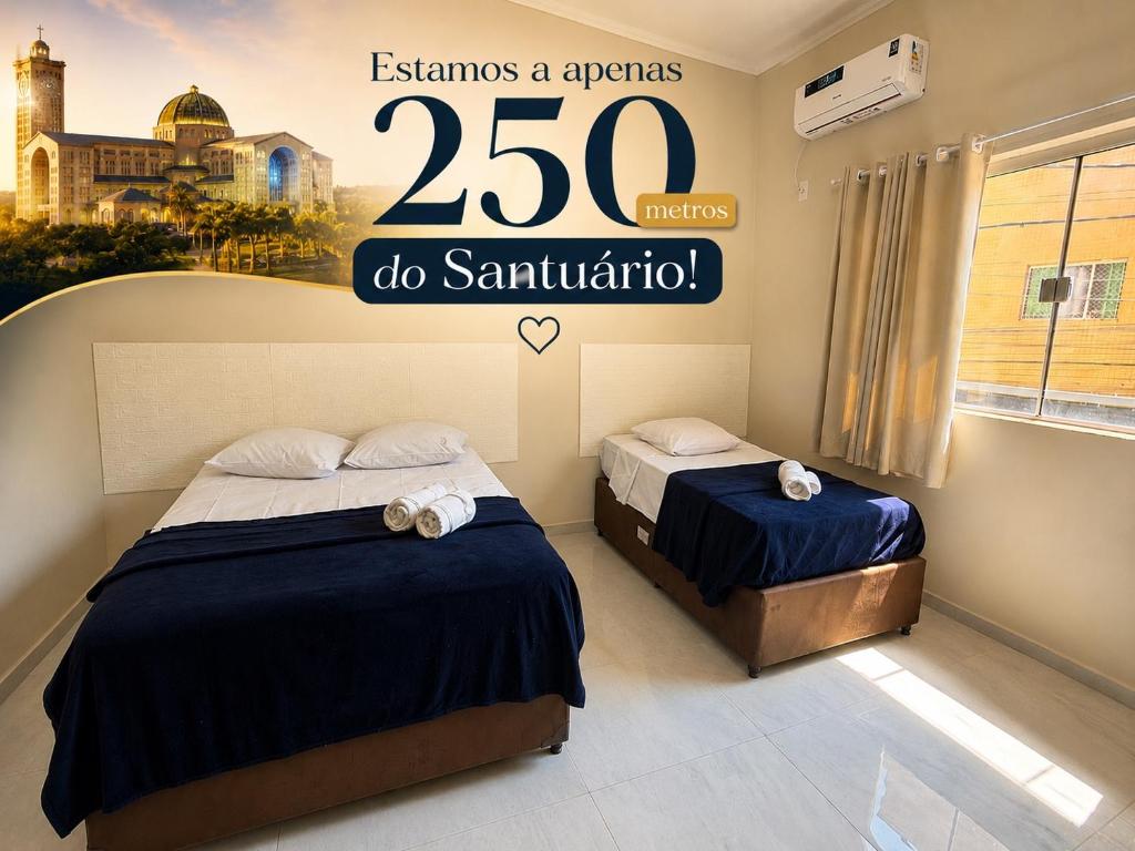 two beds in a room with a sign that reads esamos aariusz at Hotel Pousada Romanos in Aparecida