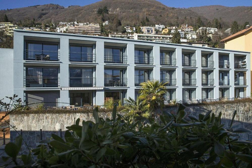a large white building with a mountain in the background at Hotel Barca Blu in Orselina