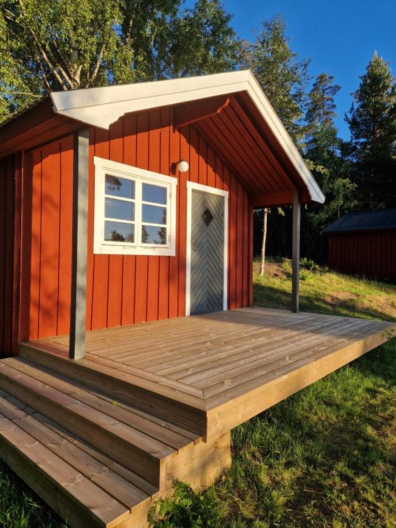 a red cabin with a deck and a window at Långseruds Stugby Nature Cabins in Byn