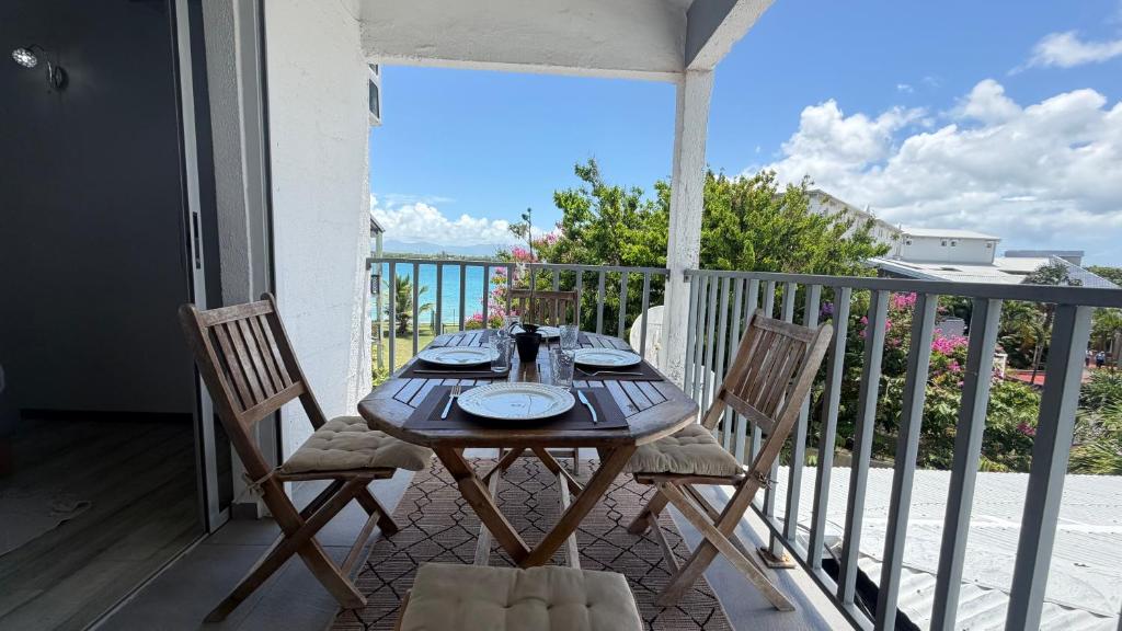 a wooden table with two chairs on a balcony at Pieds dans l eau Piscine Calme Appartement Althéa in Le Gosier