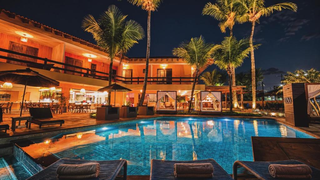 a large swimming pool with palm trees and a building at Luna Hotel Boutique - Frente à Praia in Guarujá