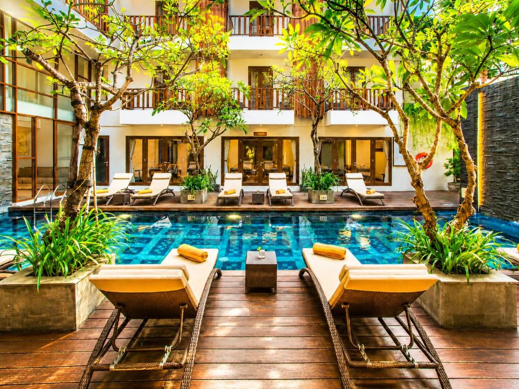 a hotel swimming pool with lounge chairs and trees at d'primahotel Seminyak in Seminyak