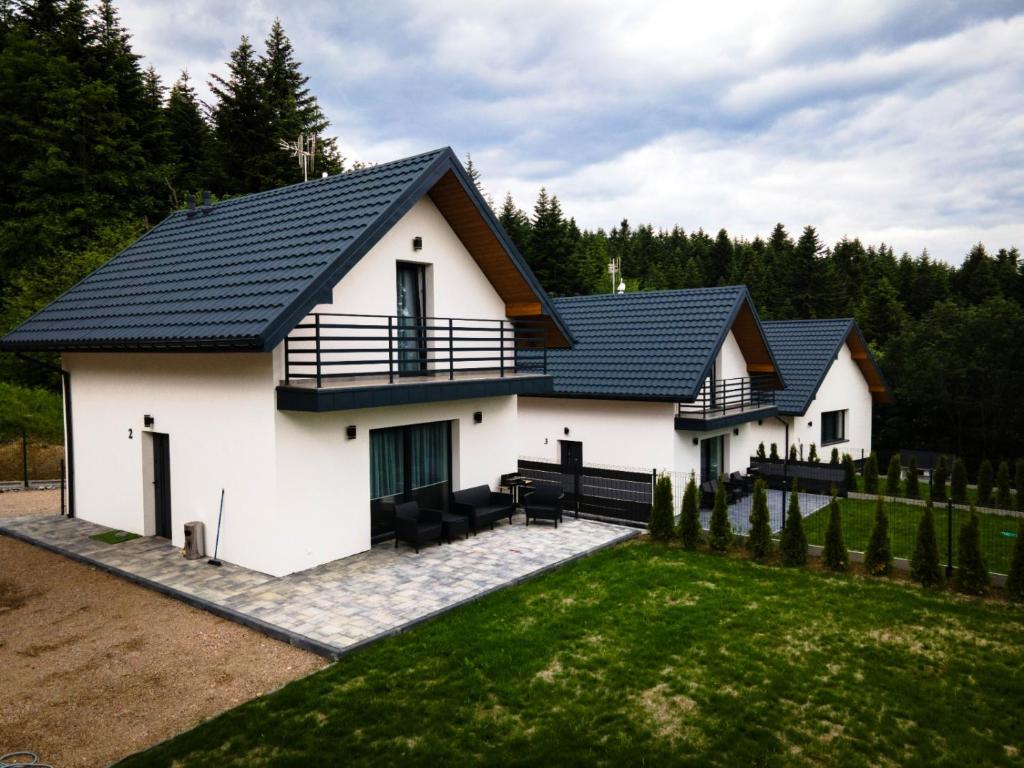 a white house with a black roof at Domki Leśne Zacisze in Baczyn