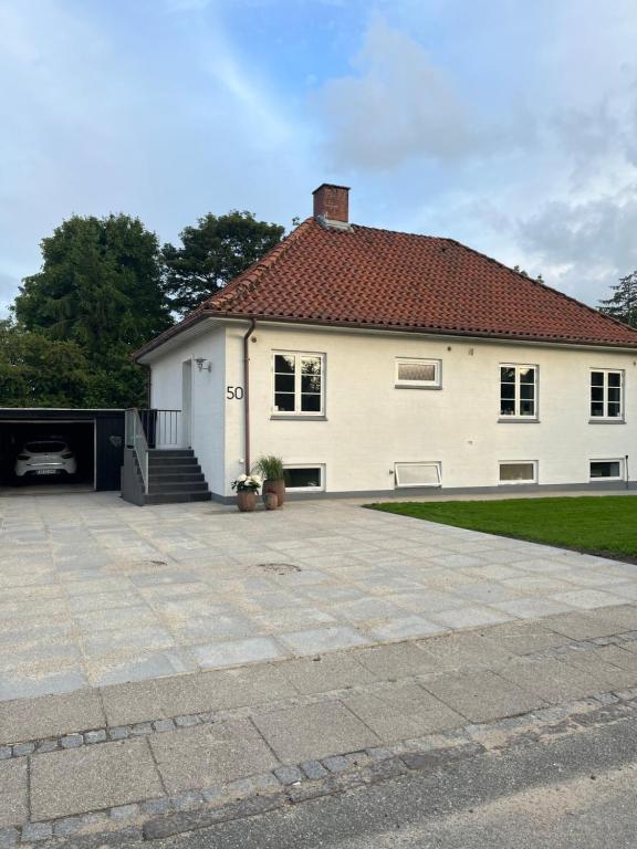 a white house with a red roof and a driveway at To værelser med dobbeltsenge tæt på E45 og banegården i Rødekro Værelserne deler bad Kælderværelser med egen indgang in Rødekro