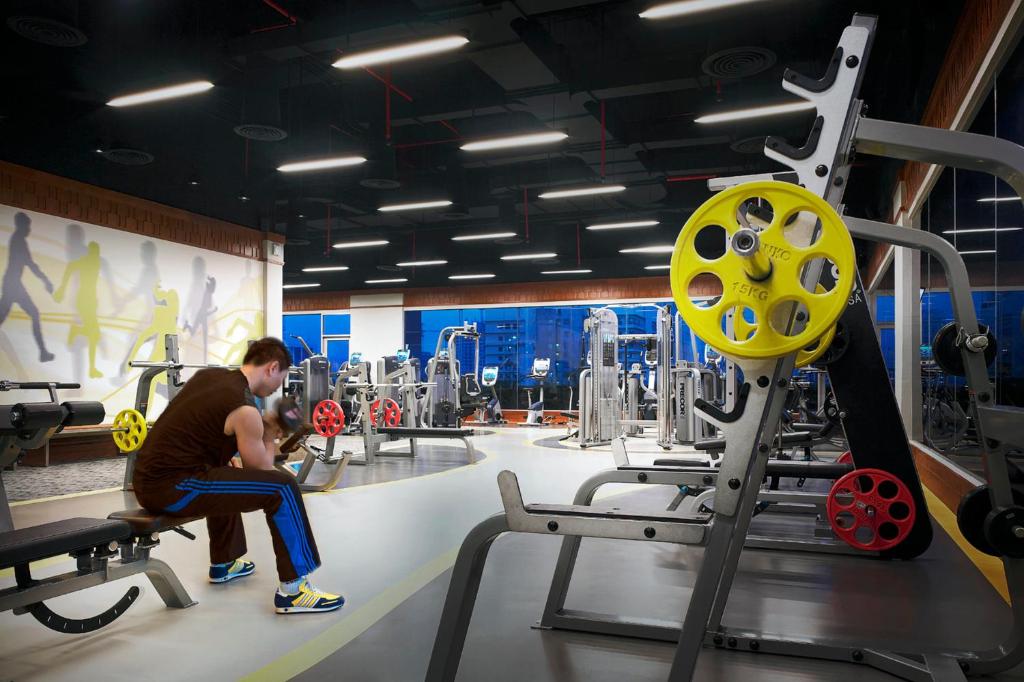 A large, brightly lit fitness room with strength equipment, benches, and weight plates.