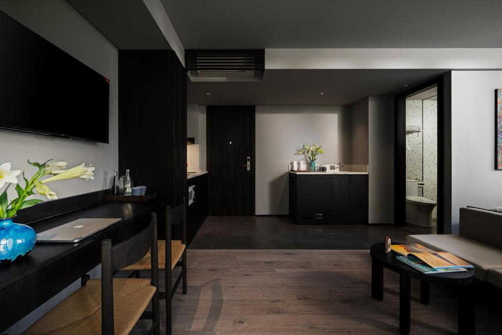 A living area with a television, dining desk, kitchenette and visible bathroom entrance.