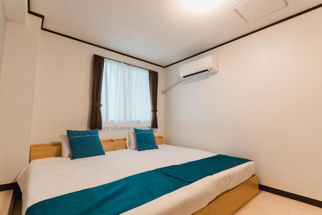 a bedroom with a bed with blue pillows and a window at Portside Stay 石垣島 離島ターミナル徒歩3分 バスターミナル前 室内リニューアル in Ishigaki Island