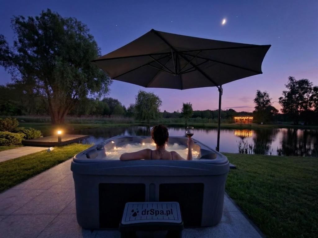 a man sitting in a bath tub with an umbrella at Słoneczny Ogród - Ekskluzywna posiadłość nad wodą, Grill i Jacuzzi in Krzywińskie